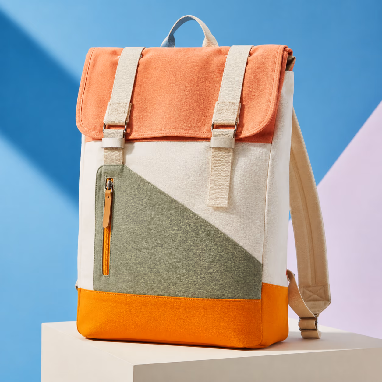 A coral, cream, sage, and orange canvas backpack displayed against a blue studio backdrop.
